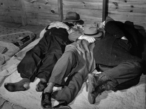 3 uomini dormono su un materasso logoro, per terra