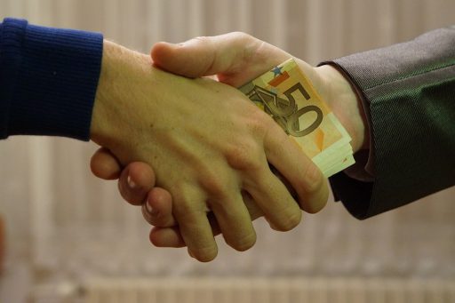 due mani che si stringono, passandosi delle banconote, in segno di corruzione